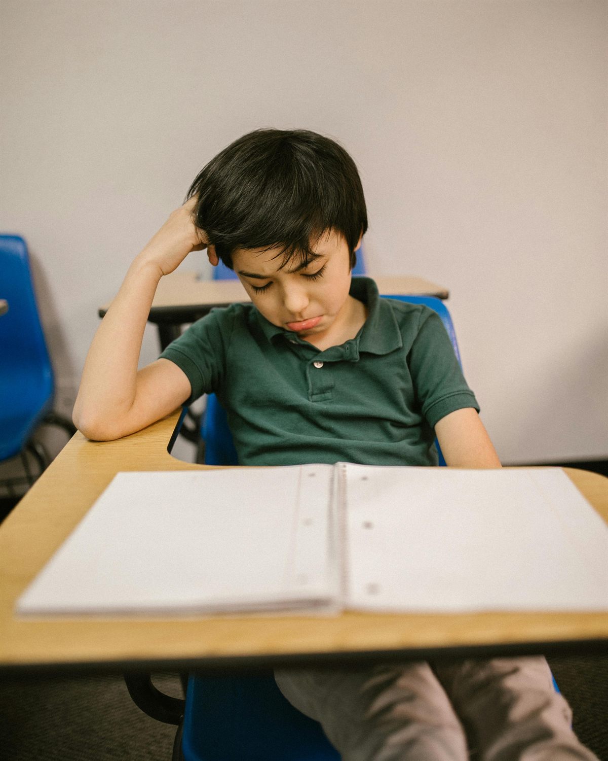 A child sitting at a desk, head in hand, looking down at a blank page